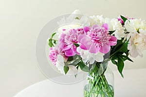 Close-up bouquet of fresh big pink, white and cream peonies in simple glass jar on glance table indoor. 