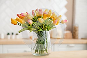 Close-up of a bouquet of fresh spring yellow tulips in a large transparent glass vase in a photo studio against the background of