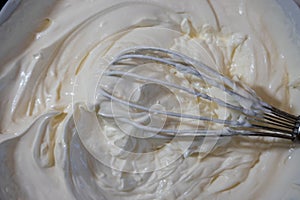 close up of a bowl of cream with whisk, texture of mascarpone soft cream cheese
