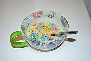 Close up of a bowl full of fruit flavored loops of sugar ready to eat breakfast cereal with a spoon sticking out