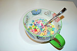 Close up of a bowl full of fruit flavored loops of sugar ready to eat breakfast cereal with a spoon sticking out