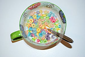 Close up of a bowl full of fruit flavored loops of sugar ready to eat breakfast cereal with a spoon sticking out