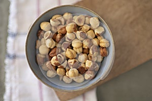 Close-up of a bowl of hazelnuts on wood board with a napkin in the background