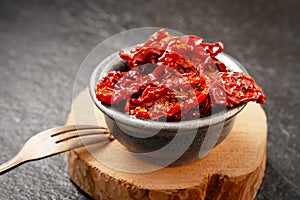 Close-up of a bowl of sun-dried tomatoes in olive oil on a gray stone background. Studio shot