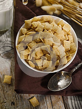 Close-up. A bowl with whole grain pads and a spoon on a brown napkin. In the background is a jug of milk. Quick breakfast cereals