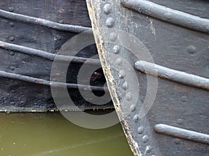 Close up of the bows of two moored old fashioned narrowboats painted black with rivets and metal hulls