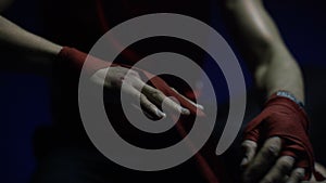 Close-up of boxer`s hand. Close-up boxer ties injured hands with red ribbon in dark locker room, preparing for training