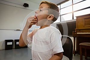 Close up of boy eating apple while standing against piano