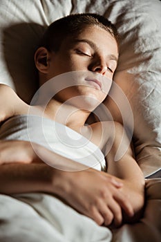 Close up on boy with folded arms asleep in bed