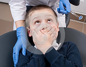 Close-up of boy frightened by dentists covers her mouth and looks for him