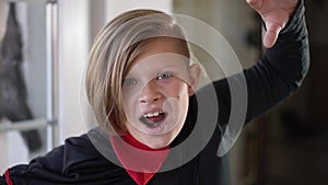 Close-up boy grimacing scaring gesturing looking at camera looking out decorated house. Caucasian child in Halloween