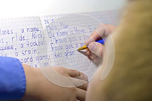 Close-up of boy hand with pencil writing english words by hand on traditional white notepad paper.