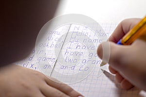 Close-up of boy hand with pencil writing english words by hand on traditional white notepad paper.