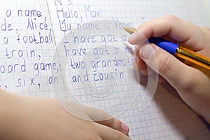 Close-up of boy hand with pencil writing english words by hand on traditional white notepad paper.