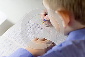 Close-up of boy hand with pencil writing english words by hand on traditional white notepad paper.