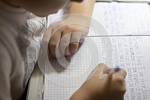 Close-up of boy hand with pencil writing english words by hand on traditional white notepad paper.