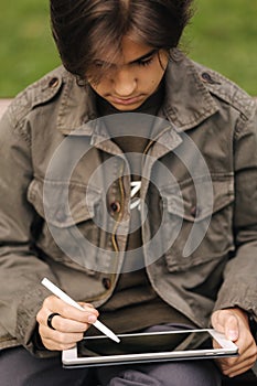 Close-up of boy painting in tablet using pencil. Young designer using tablet outdoor. Autumn time