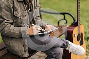 Close-up of boy painting in tablet using pencil. Young designer using tablet outdoor. Autumn time. Background of guitar