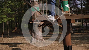 A close-up of a boy in sneakers in an adventure park is climbing on a rope road.