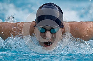 Close up of Boy swimming butterfly stroke with face in water spray and sun highlights