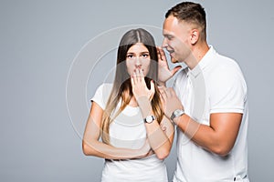 Close up of boyfriend whispering secrets to girlfriend isolated on gray background