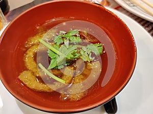 Close up of braised fish maw in red gravy serving in red bowl. Traditional Chinese food. Popular in Thailand