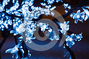 Close-up of branch artificial tree with LED flowers cherry, blue light garland, selective focus