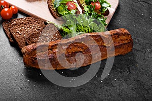 Close-up of a bread on a table background. A cut, crunchy dark baguette and a cutting desk with vegetable sandwiches.