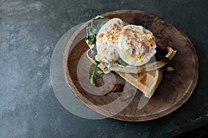 Close up Breakfast with Poached Egg on waffle with spinach and bacon on wooden texture plate on grey stone table. Top