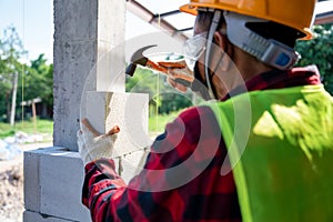 Close-up of bricklayer builder use a hammer to help with autoclaved aerated concrete blocks. Walling, installing bricks on