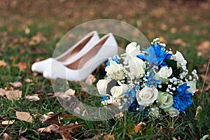 Close-up of bridal yellow rose bouquet on background of her white shoes on green grass