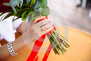 Close-up of bride hands holding beautiful wedding bouquet with red and pink roses. Concept of floristics and jewellery.