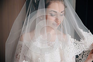 A close-up of the bride put on a veil. The face of a beautiful girl through a white lace fabric.