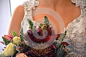 Close up of bride`s chest white beaded ornate dress with jewel colored flower bouquet