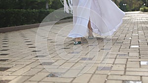 Close-up of the bride's feet in green shoes, walking with a confident step along the path in the park.