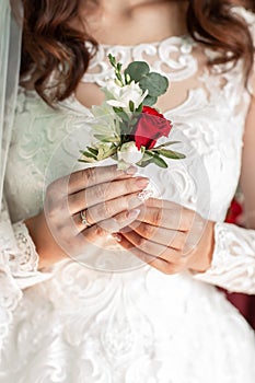 Close-up of the bride`s hands holds a boutonniere. boutonniere with red rose.Beautiful sensual bride holding stylish boutonniere