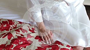 Close-up of the bride in a satin negligee sitting on the bed in the hotel.