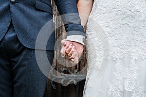 Close up of bride in white dress and groom in suit just married holding hands together following wedding ceremony stood in doorway