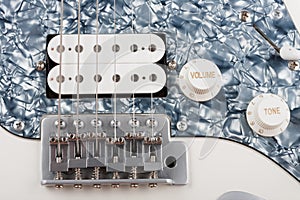 Close up of bridge and  humbucker and controls on white white electric guitar, studio shoot