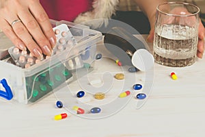 Close-up of bright colored medical pills and capsules with medicines and a glass of water next to them. The woman takes out the