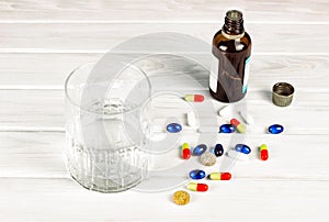 Close-up of bright colored medical tablets, a bottle of medicine and capsules with medicines and a glass of water. Scattered on
