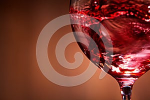 Close-up of brightly red wine poured in the wineglass and abstract splashing against brown background.