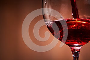 Close-up of brightly red wine poured in the wineglass and abstract splashing against brown background.