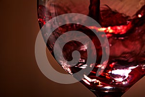Close-up of brightly red wine poured in the wineglass and abstract splashing against brown background.