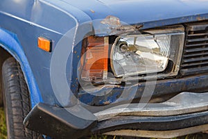 broken blue car with broken headlight and wing on the car is dented.