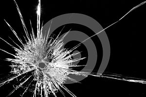 Close up of broken, cracked pane of glass with bullet hole, on black background with copy space