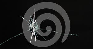 Close up of broken, cracked pane of glass with bullet hole, on black background with copy space