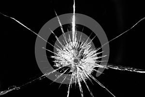 Close up of broken, cracked pane of glass with central bullet hole, on black background