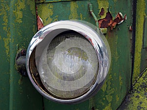 Close up of the broken headlight of an old abandoned truck with rusted green paintwork