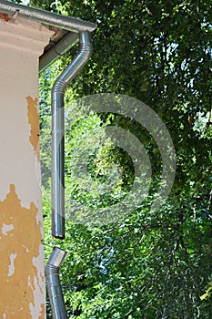 A close-up of a broken metal roof gutter, damaged downpipe, downspout of an old house that needs renovation, roof gutter to be